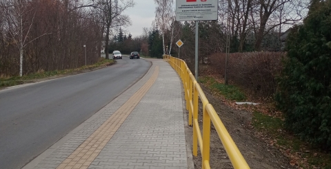 Chodnik i przejście dla pieszych w Grzebienisku. Przy chodniku stoi tablica informująca o dofinansowaniu inwestycji.
