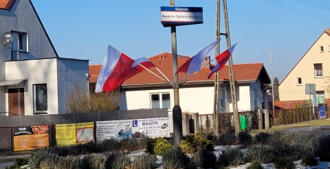 Biało-czerwone flagi zawieszone na słupie z oznaczeniem ronda imienia Żołnierzy Wyklętych.