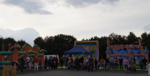Dmuchane zjeżdżalnie i labirynt dla dzieci na placu przed biblioteką w Dusznikach podczas Dożynek Gminnych 2021. Na pierwszym planie rodzice dzieci korzystających z zabaw.  