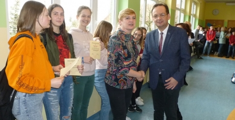 Na zdjęciu Wójt Gminy Duszniki ściska dłoń nauczycielki szkoły podstawowej w Dusznikach w otoczeniu wyróżnionych uczniów szkoły.